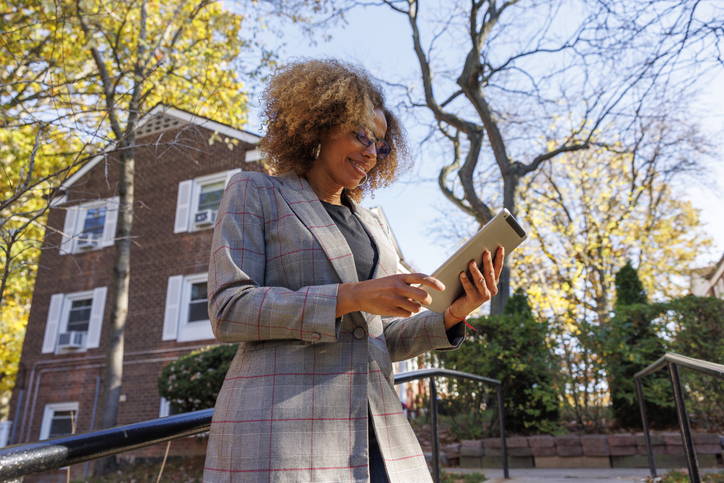 Real estate agent (REALTOR®) walking away from home and using tablet.